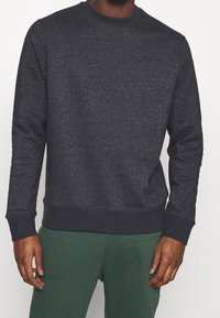 Mörkgrå sweatshirt med rund hals, långa ärmar och ribbade muddarna och fållen. Tillverkad av ett mjukt, texturerat tyg. Ingen synlig märkning.