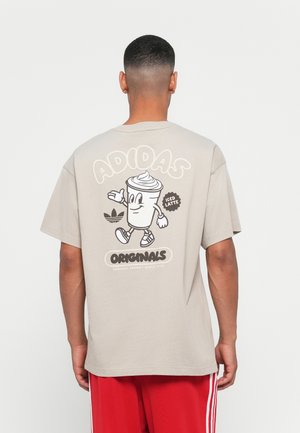 Beige pamut póló, hátán egy rajzfilmszerű jeges latte grafikával, kontrasztos színekben "ADIDAS" és "ORIGINALS" felirattal.