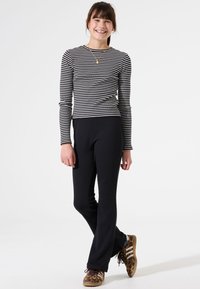 Gestreepte lange mouwen top in zwart en wit, gecombineerd met zwarte, strakke broek. Schoeisel met een bruine en gouden dierenprint.