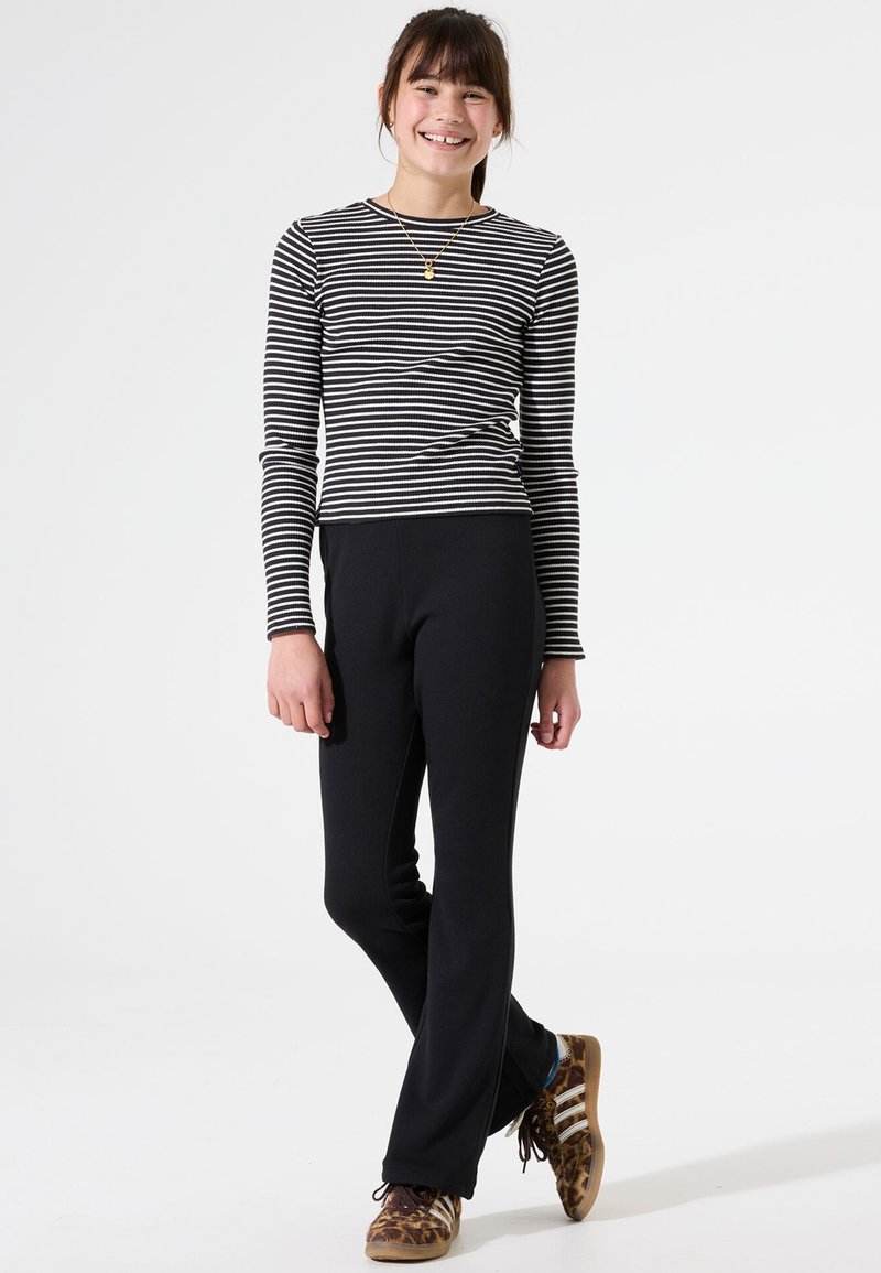 Gestreepte lange mouwen top in zwart en wit, gecombineerd met zwarte, strakke broek. Schoeisel met een bruine en gouden dierenprint.