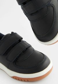 Granatowe skórzane buty z dwoma rzepami, zaokrąglonym noskiem, białą podeszwą środkową i brązową podeszwą z gumy, z przeszyciami.