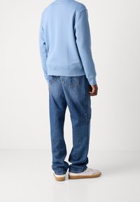 Sudadera azul clara con dobladillo acanalado, combinada con vaqueros azules de pierna recta y zapatillas blancas con suelas color chicle. Bolsillos traseros visibles en los vaqueros.