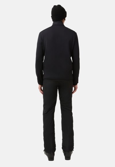 Zwarte slim-fit jas met hoge kraag, gecombineerd met zwarte slim-fit broek en een gebreide beanie. Strak ontwerp, gladde textuur, minimale details.