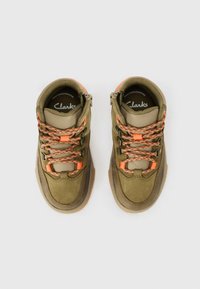 Chaussures de randonnée vertes en suede et en tissu avec des accents orange et des lacets à motifs. Comprend un design montante et une fermeture éclair sur le côté pour un accès facile.