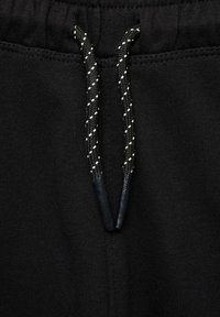 Svarta joggerbyxor i ett strukturerat fleece-material, med en dragsko med snurrmönster och svarta spetsar. Inkluderad elastisk midja.