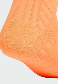 Calcetín naranja brillante con acabado texturizado y diseño acanalado, con refuerzo en el talón para mayor durabilidad.