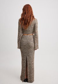 Abito lungo in maglia marrone attillato con uno spacco alto sul retro, caratterizzato da maniche lunghe e un design a top corto. Dettagli in tessuto strutturato.