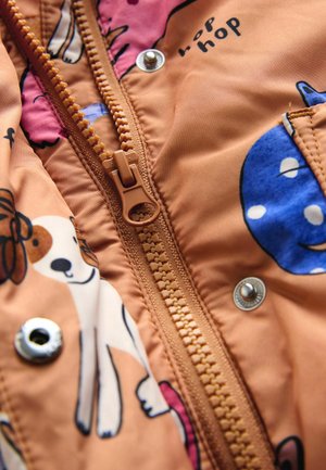 Oranž kangas loomamustritega, mille keskel on tõmblukk, metallist trukknupp ja servade mööda nähtavad õmblused.