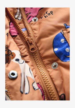 Oranžna tkanina z živalskimi potiski, z osrednjim zadrgo, kovinskim drukom in vidnimi šivi ob robovih.