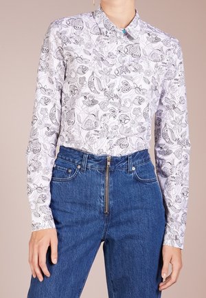 Hvid langærmet skjorte med sorte detaljerede blomster- og dyremønstre, kombineret med højtaljede blå jeans med lynlås foran.