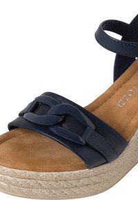 Sandaletta con zeppa blu navy con una soletta in suede, accentata da una catena sulla fascetta e una suola in stile juta texturizzata. Costruzione in pelle liscia.