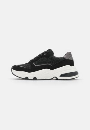 Zwart-grijze sneaker met een gestructureerd bovenwerk, vetersluiting en een stevige witte zool met zwarte accenten voor stabiliteit en comfort.