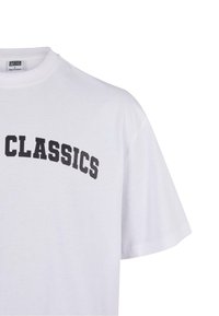 Balta medvilninė marškinėliai trumpomis rankovėmis, su juodu tekstu, užrašytu „CLASSICS“ drąsiu, išlenktu šriftu per krūtinę.