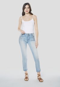 Witte mouwloze top gecombineerd met lichtblauwe slim-fit spijkerbroek met borduursels, die iets boven de enkel valt, en bruine sandalen met bandjes.