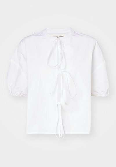 Blusa bianca con maniche a sbuffo realizzata in tessuto leggero, caratterizzata da una chiusura con laccio al collo e una vestibilità leggermente ampia per un maggiore comfort.