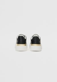 Black leather sneakers with white soles, featuring a gold accent on the heel. Rounded shape with a low-top design and padded collar.