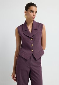 Sleeveless burgundy blazer with a notched collar, five gold buttons, and side pockets, paired with matching trousers for a cohesive look.