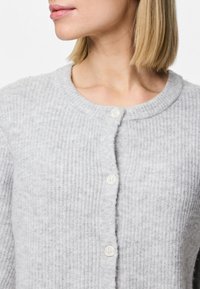 Šedý žebrovaný kardigan vyrobený z měkké látky, disponující kulatým výstřihem a třemi bílými knoflíky vpředu pro zapínání.
