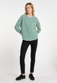 Maglia a maniche lunghe a righe verdi e bianche con scollo rotondo e taschino sul petto, abbinata a pantaloni neri slim-fit e scarpe nere.