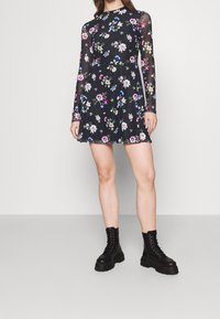 Vestido negro con estampado floral, mangas largas y transparentes, falda acampanada, y combinado con botas de combate negras con cordones.