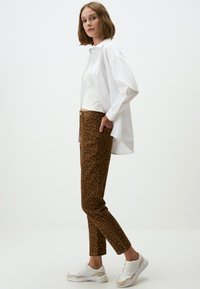 Pantalons imprimé léopard marron avec une coupe ajustée, portés avec un haut moulant blanc et une chemise blanche ample, accompagnés de sneakers blanches.