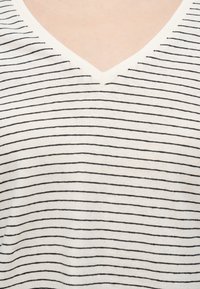 Λευκό πουκάμισο με V-λαιμόκοψη και λεπτές μαύρες οριζόντιες ρίγες στο άνω μέρος του στήθους και το λαιμό ενός προσώπου.