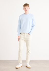 Lichtblauwe trui met een ronde hals, beige slim-fit broek en witte sneakers met beige accenten. Vriendelijke texturen, casual ontwerp.