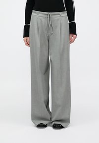 Hallid laia lõikega püksid, valmistatud sarnasest kangast, millel on ees voldid, nöörist vöökoht ja peen läige, sobituvad mustade kingadega.