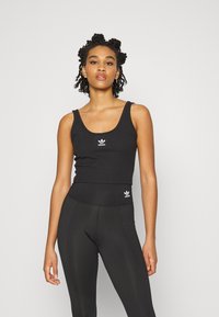 Top cropped a costine nera e leggings a vita alta, entrambi con il logo Adidas bianco. Texture liscia, design aderente.
