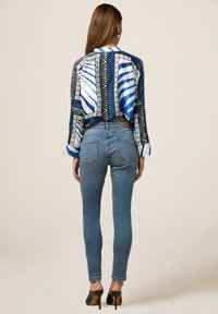 Blusa de patrón azul y negro con mangas largas, combinada con jeans ajustados de mezclilla azules y mule de tacón negro. Diseño limpio y ajuste estructurado.