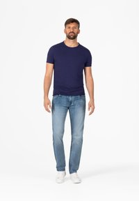 Marineblauwe t-shirt met korte mouwen, gestructureerde stof, gecombineerd met lichtblauwe recht-toe-rechtaan jeans en witte sneakers, staand op een effen achtergrond.