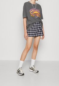 Šedé grafické tričko s logem Billabong, spárované s námořnickou kostkovanou mini sukní. Bílá crew ponožky a vícebarevné sportovní boty dotvářejí vzhled.