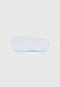 Sole di sneaker bianca con motivi di battistrada e logo Nike integrato, fotografata su uno sfondo chiaro e semplice.