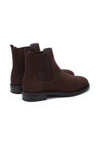 Bottines en suède marron avec panneaux latéraux en élastique et bout rond lisse. Semelle en caoutchouc noir avec un léger talon. Design simple sans logos visibles.