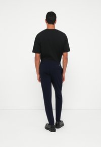 T-shirt preto de mangas curtas emparelhado com calças azul-marinho. As calças apresentam uma textura suave, cintura elástica e um bolso traseiro. Sapatos pretos completam o visual.