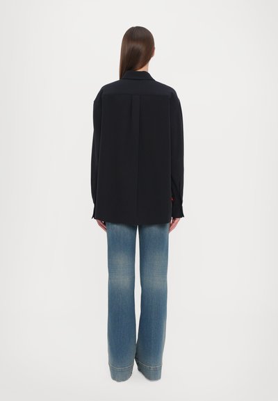 Maglietta nera a maniche lunghe con colletto, vestibilità comoda e piega sul retro, abbinata a jeans a gamba larga azzurri chiari con un lavaggio sbiadito e orlo sfrangiato.