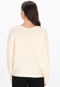 Crème-kleurig gebreid sweater met een chevronpatroon, losse pasvorm, diepe V-hals en geribde manchetten, gedragen met zwarte broek.