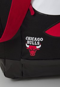 Schwarzer Rucksack mit roten Trägern und einem weißen Chicago Bulls-Logo, das ein Bullenkopf zeigt. Der Text lautet "CHICAGO BULLS" in Weiß.