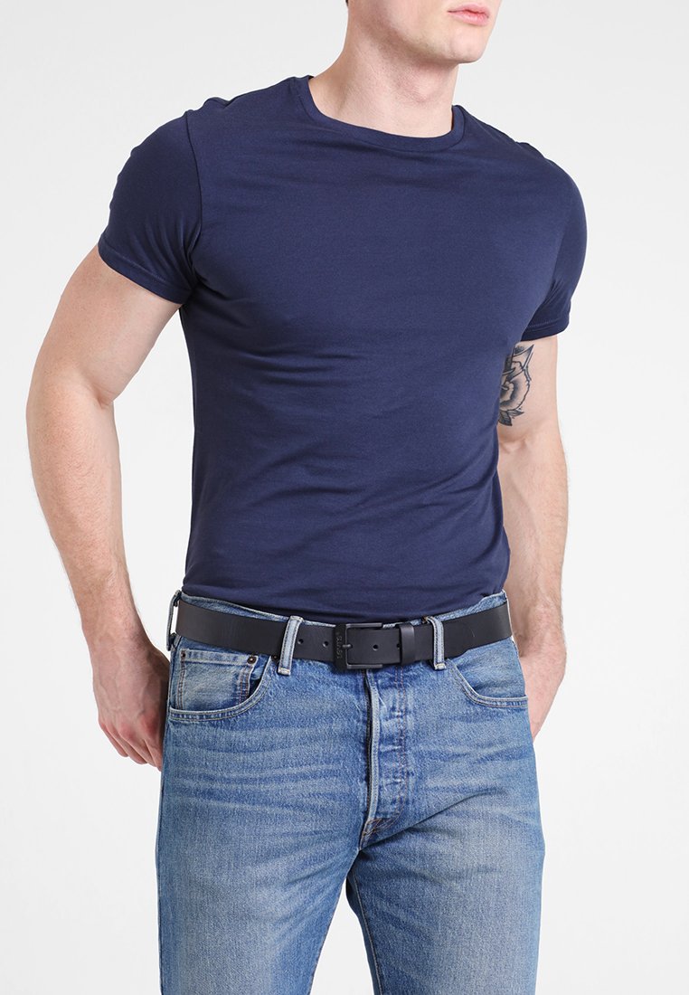 T-shirt ajusté bleu marine à manches courtes porté avec un jean bleu clair et une ceinture noire. Tissu lisse, col rond simple, design classique.