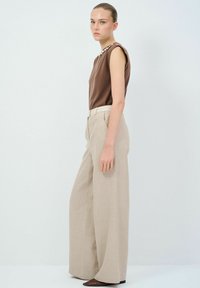 Bruine mouwloze top met schouderdetails, gecombineerd met hoge beige wijde broek en spitse bruine ballerina's. Minimalistisch ontwerp.