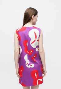 Αμάνικο φόρεμα σε μωβ ύφασμα με μεγάλα κόκκινα και λευκά λουλουδένια σχέδια. Περιλαμβάνει φερμουάρ στο πίσω μέρος και άνετη γραμμή.