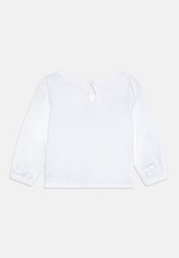 Top bianco a maniche lunghe con scollatura rotonda, chiusura a bottone sul retro e polsini arricciati. Realizzato in morbido cotone.