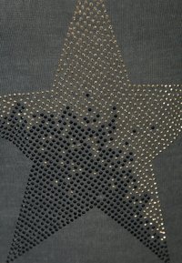 Dunkelgrauer Stoff mit einem großen Stern, der aus metallischen schwarzen und goldenen Nieten besteht, und einem Verlauf von solider zu spärlicher Detailierung.