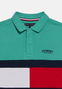 Τιρκουάζ πόλο πουκάμισο με γιακά, με οριζόντιες ρίγες σε ναυτικό μπλε, κόκκινο και λευκό. Κεντημένο λογότυπο "TOMMY HILFIGER" στο αριστερό στήθος.