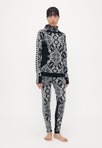 Svart og hvit mønstret langermet topp med høy krage og matchende leggings med blomster- og geometriske design.