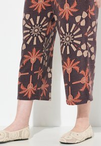 Bruna croppade byxor med röd och beige palm- och solstrålemönster, i kombination med ljusbeige virkade flats. Strukturerad tyg, avslappnad passform.