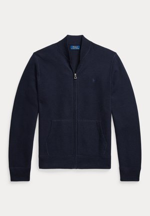 Cardigan bleu marine zippé avec manches longues, poches avant, poignets et ourlet côtelés, et une étiquette Polo Ralph Lauren à l’intérieur du col.