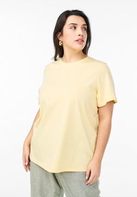 Ljusgul bomulls-t-shirt med rund hals och korta ärmar, med en avslappnad passform och mjuk textur. Matchad med gröna lösa byxor.