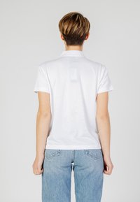Polo bianco con colletto e maniche corte, realizzato in tessuto liscio. Taglio classico, orlo dritto. Indossato con jeans azzurri.