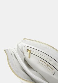 Borsa a tracolla in pelle bianca con zip dorata, tasca interna per carte e patch con logo. Texture liscia e design minimalista.